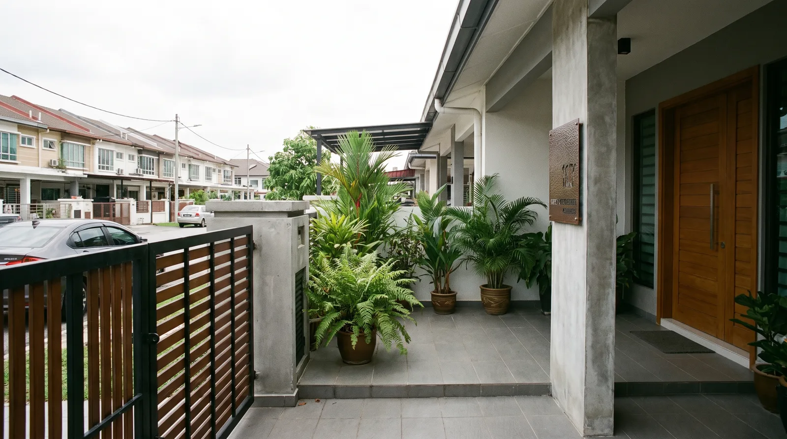 front gate and porch of a modern Malaysian terrace house with a mounted house number plate beside the door