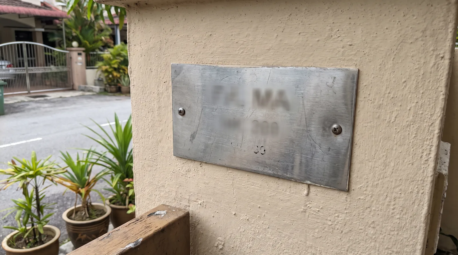 close-up of a brushed stainless steel house number plate mounted on a rendered exterior wall in daylight