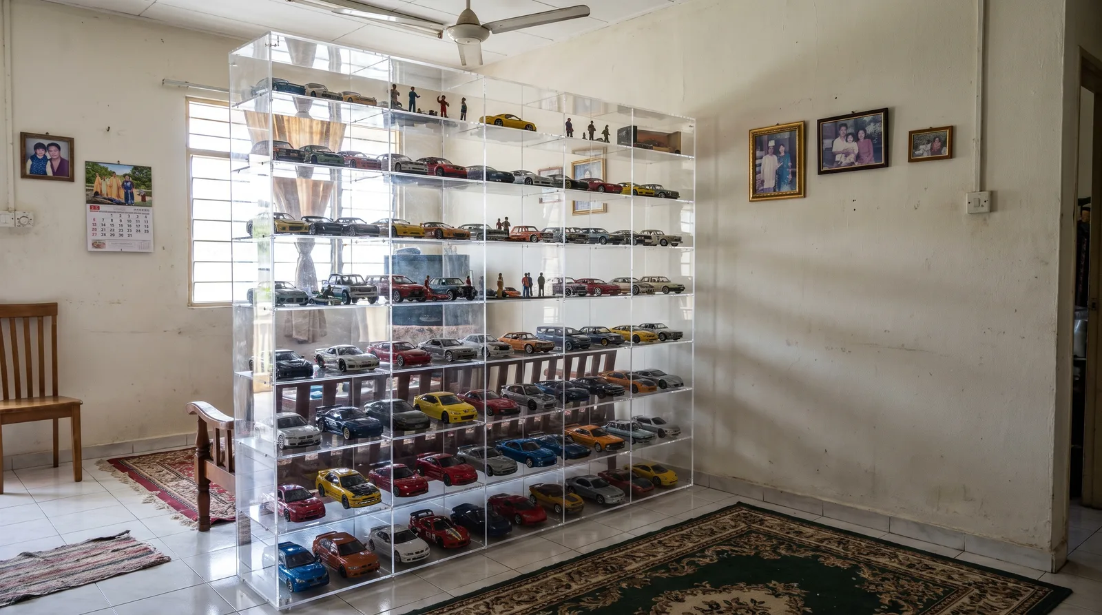 tall multi-tier acrylic display cabinet against a wall in a Malaysian home, filled with model cars and figures