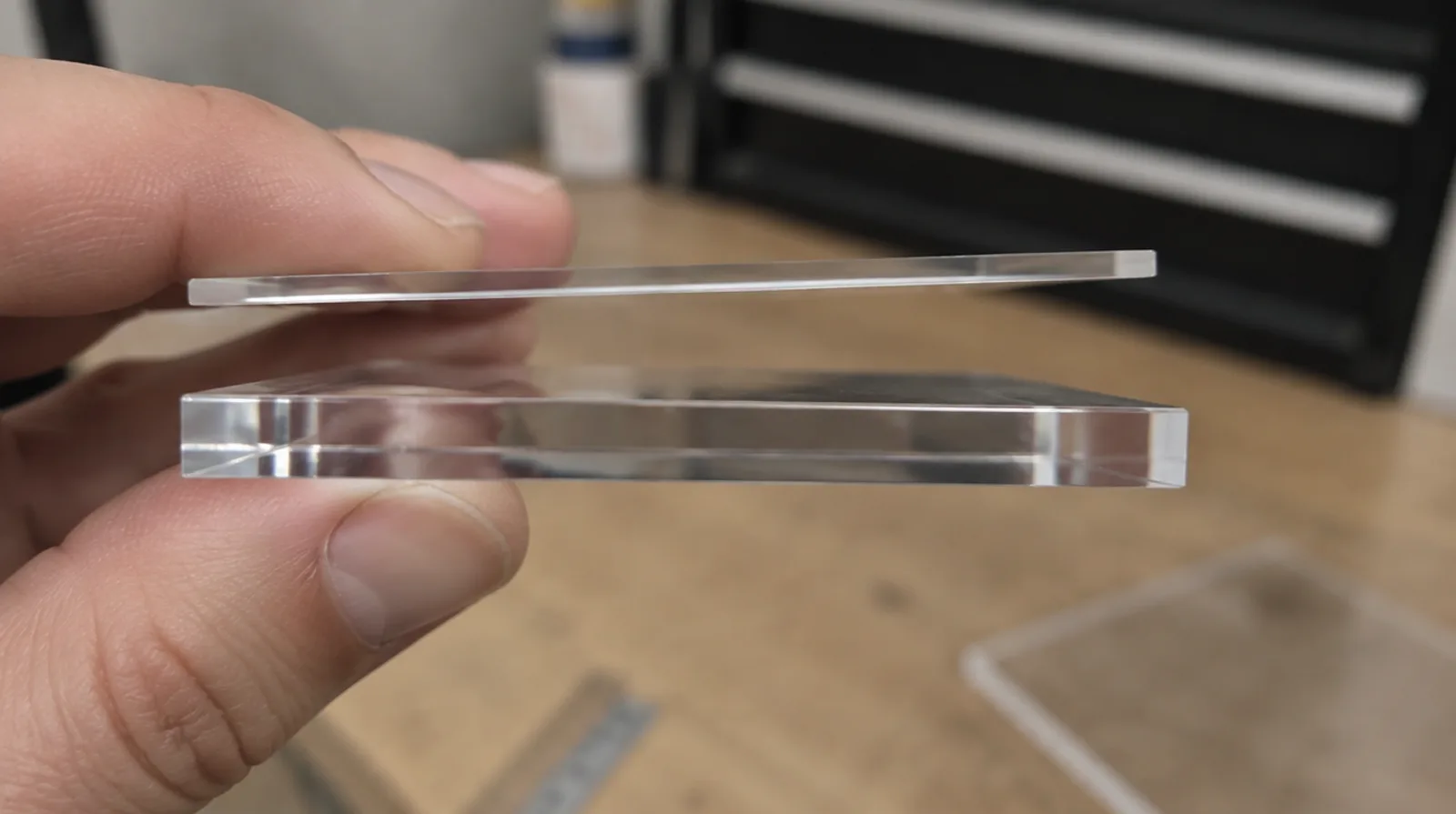 Two clear acrylic sheet edges of different thickness held side by side for comparison