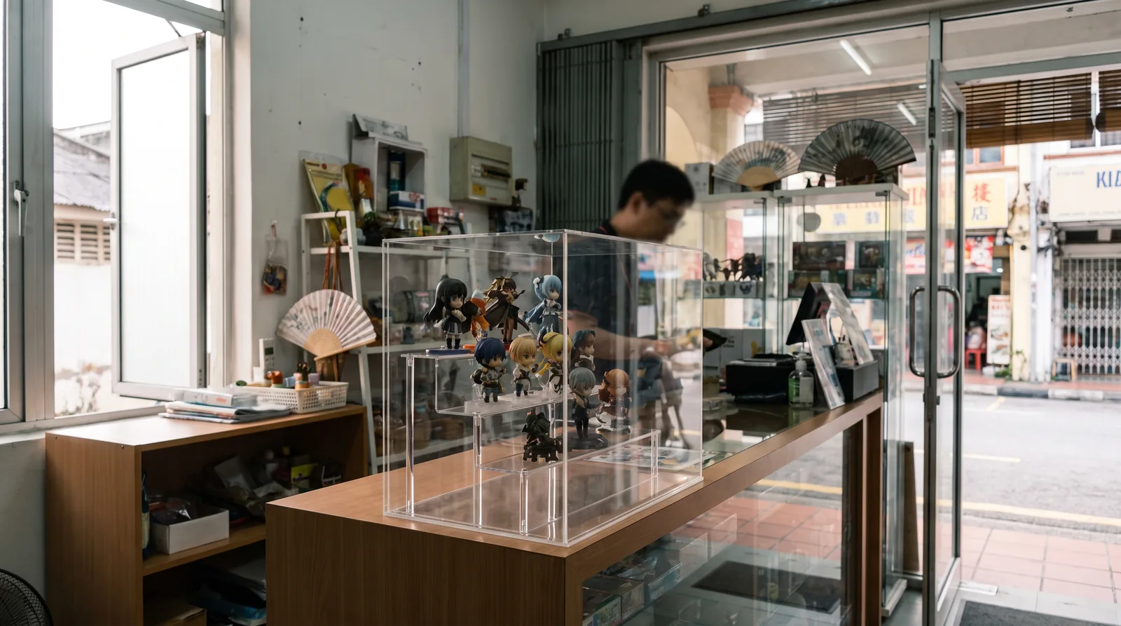 clear acrylic display case on a retail counter holding collectible figurines, softly lit shop interior