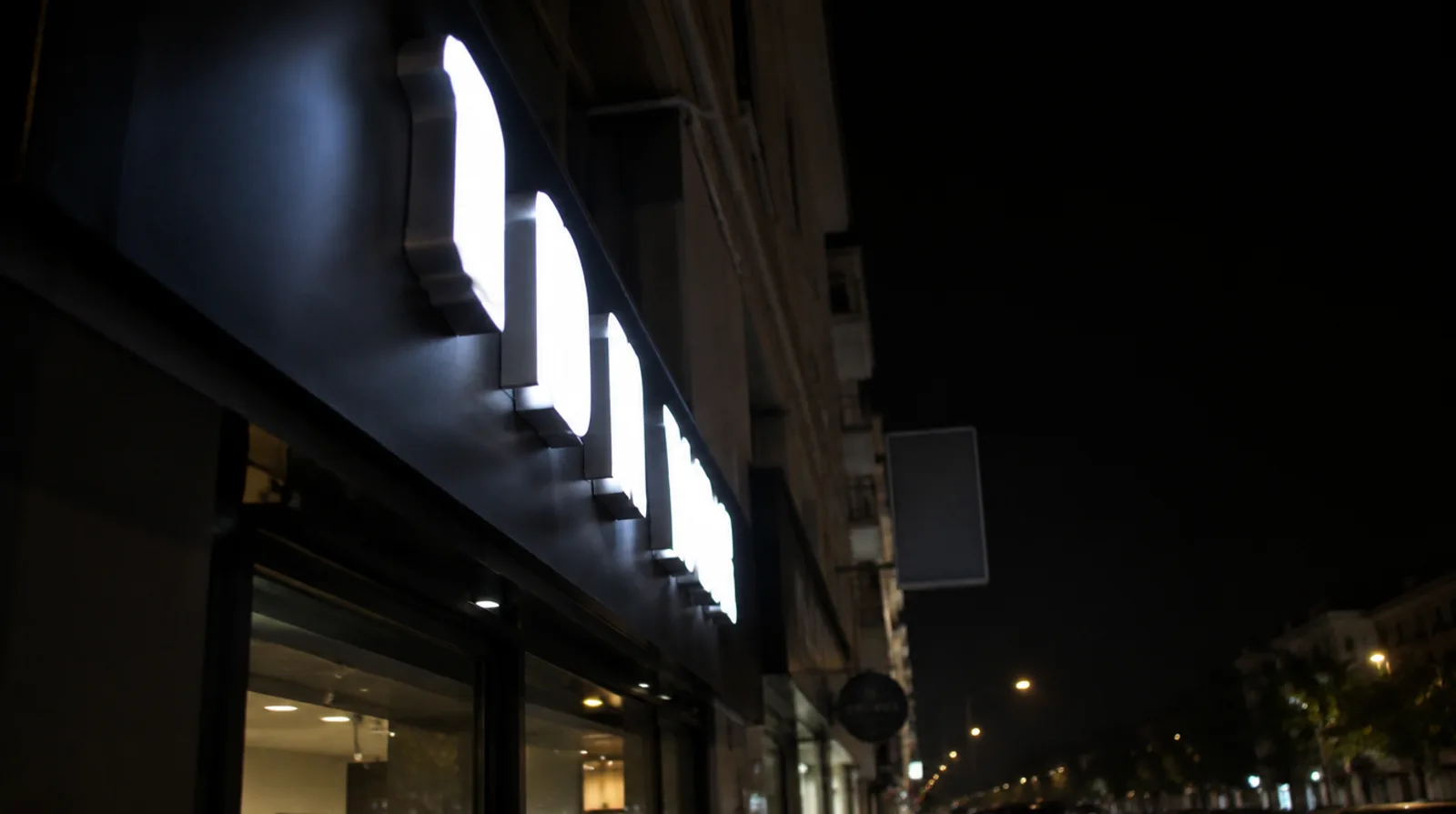 Front-lit LED channel letters glowing white through acrylic faces on a dark shop fascia at night