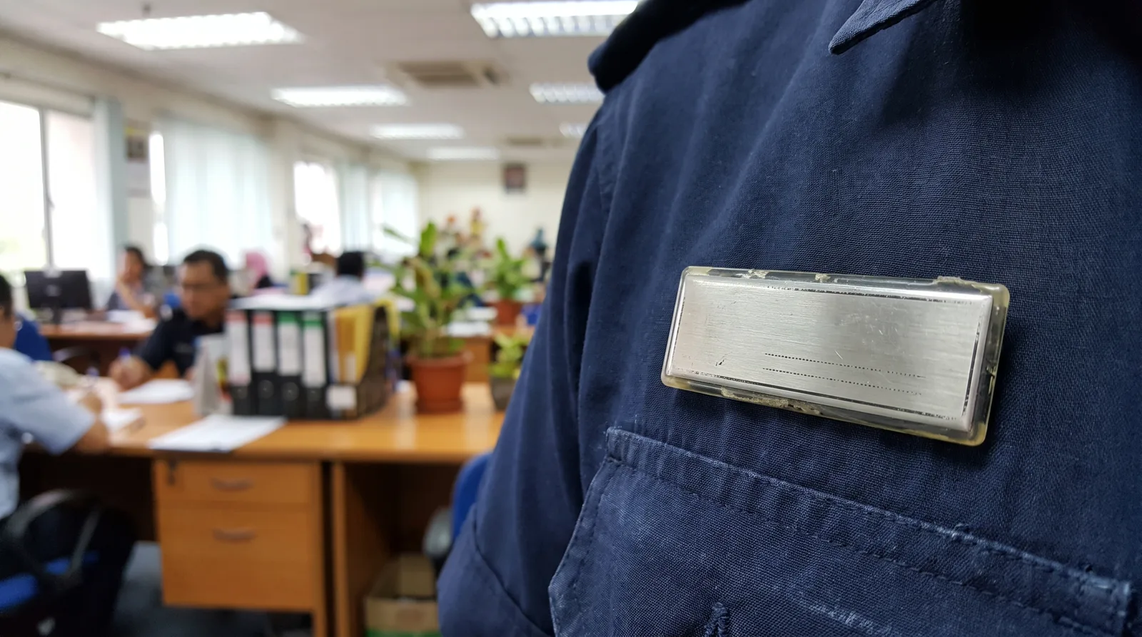 close-up of a staff name badge pinned to a dark uniform shirt, shallow background of an office