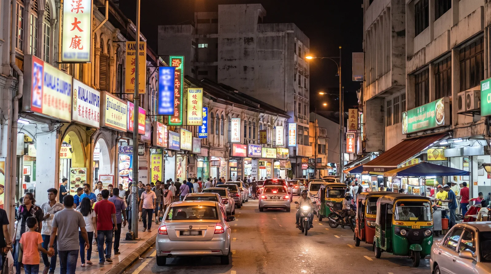 busy Malaysian commercial street at night, shopfront signs glowing along both sides of the road