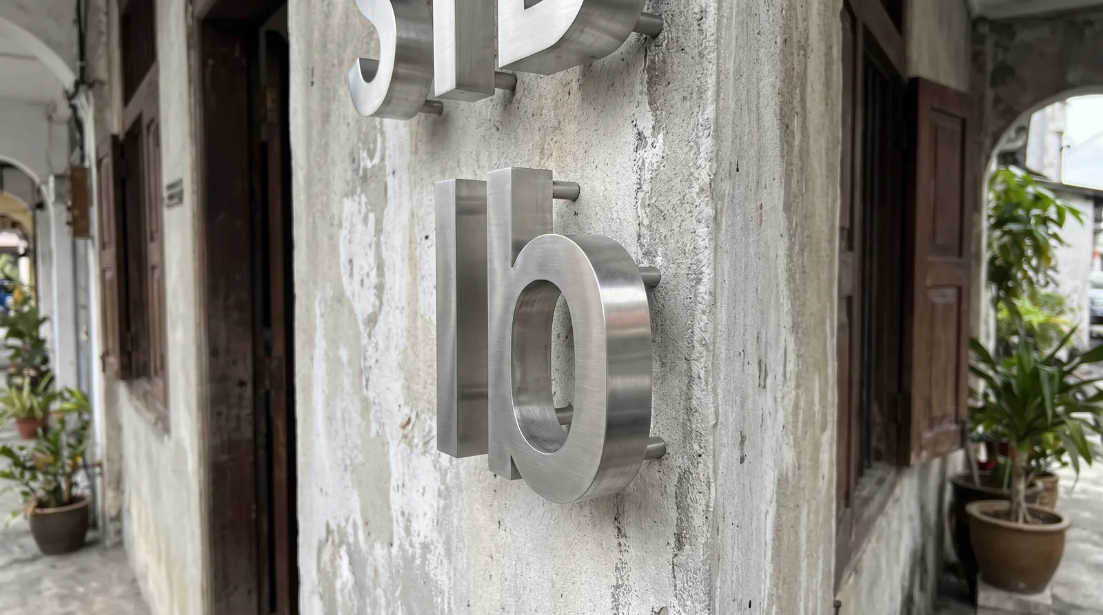 angled close-up of brushed stainless steel three-dimensional letters mounted on a rendered wall, showing the depth of th
