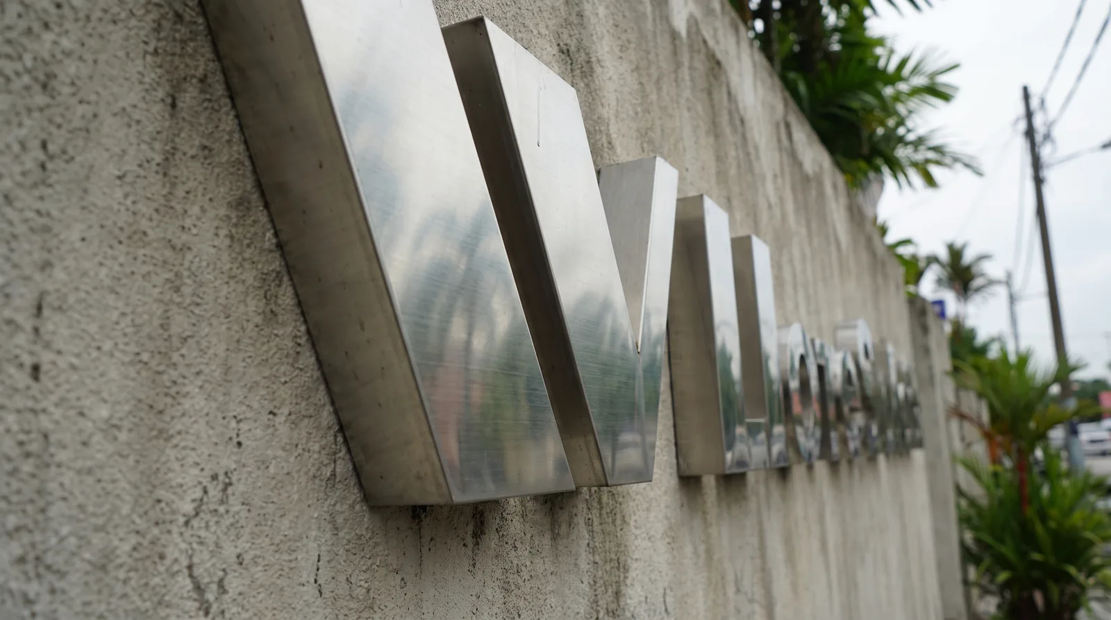 angled close-up of brushed stainless steel three-dimensional letters mounted on a rendered wall, showing the depth of th