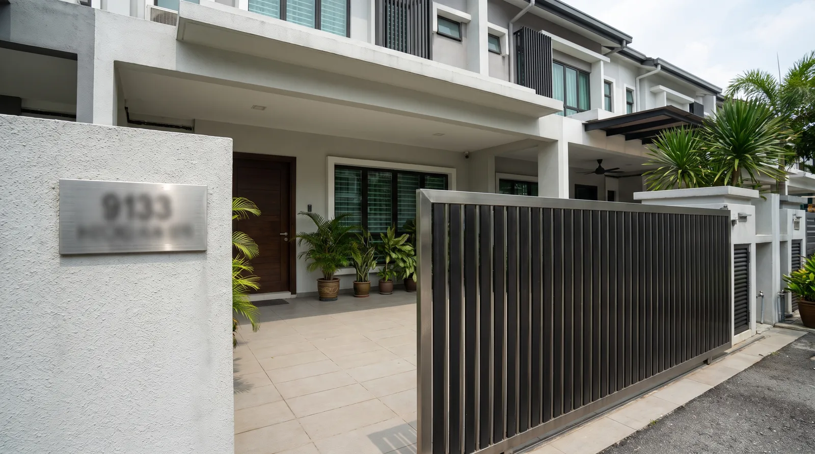 front porch and gate of a modern Malaysian terrace house with a brushed metal house number plate mounted on the rendered