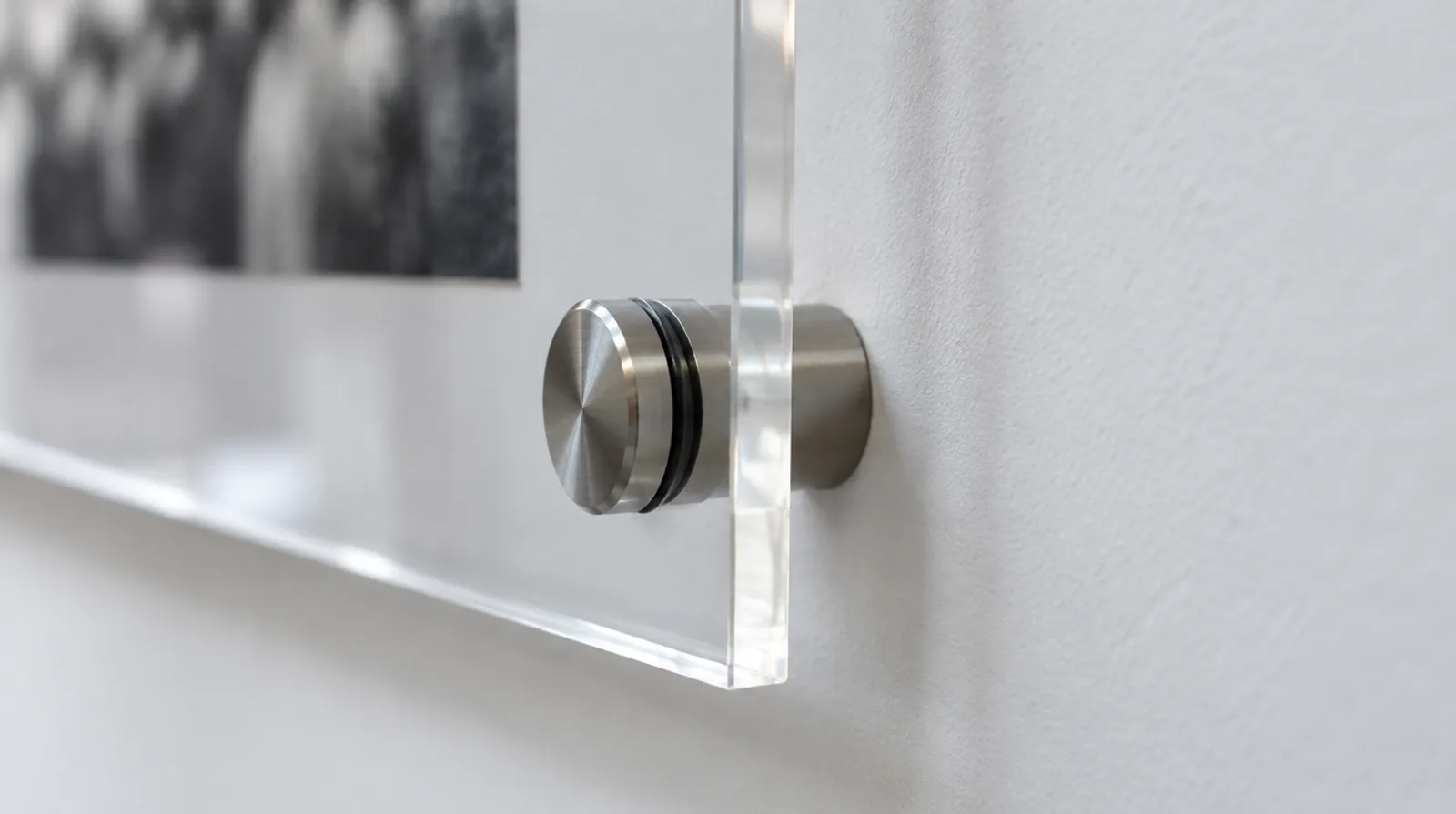 Stainless steel standoff spacer holding the corner of a clear acrylic panel away from a white wall