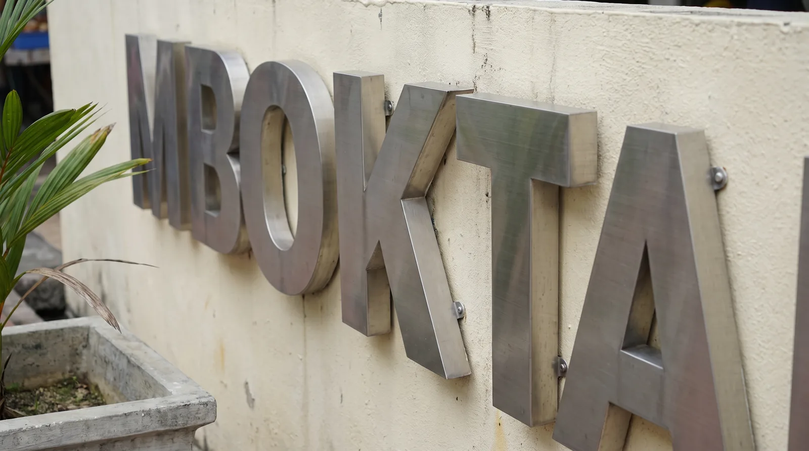 angled close-up of brushed stainless steel three-dimensional letters mounted on a rendered wall, showing the depth of th
